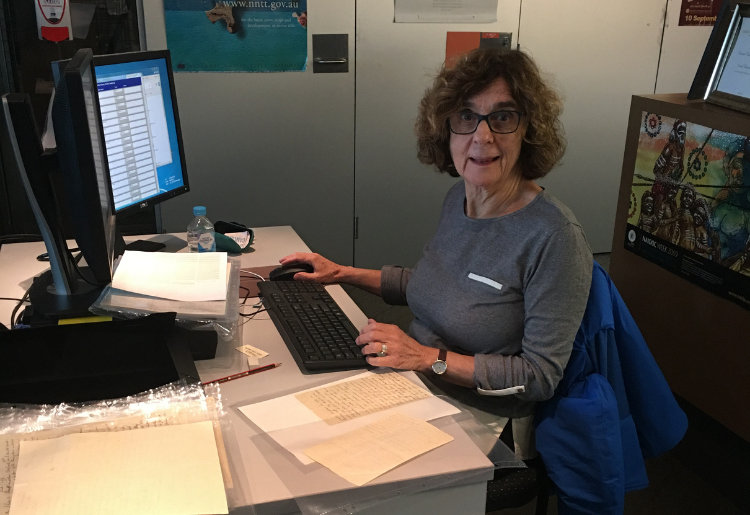 Peggy Brock smiling for the camera. She is sitting at her desk, in front of her computer at the South Australian Museum. 